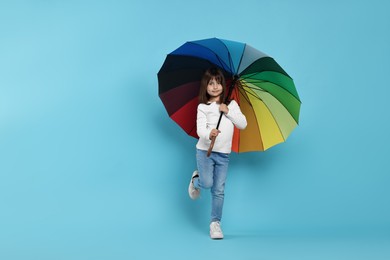 Photo of Cute little girl with colorful umbrella on light blue background. Space for text