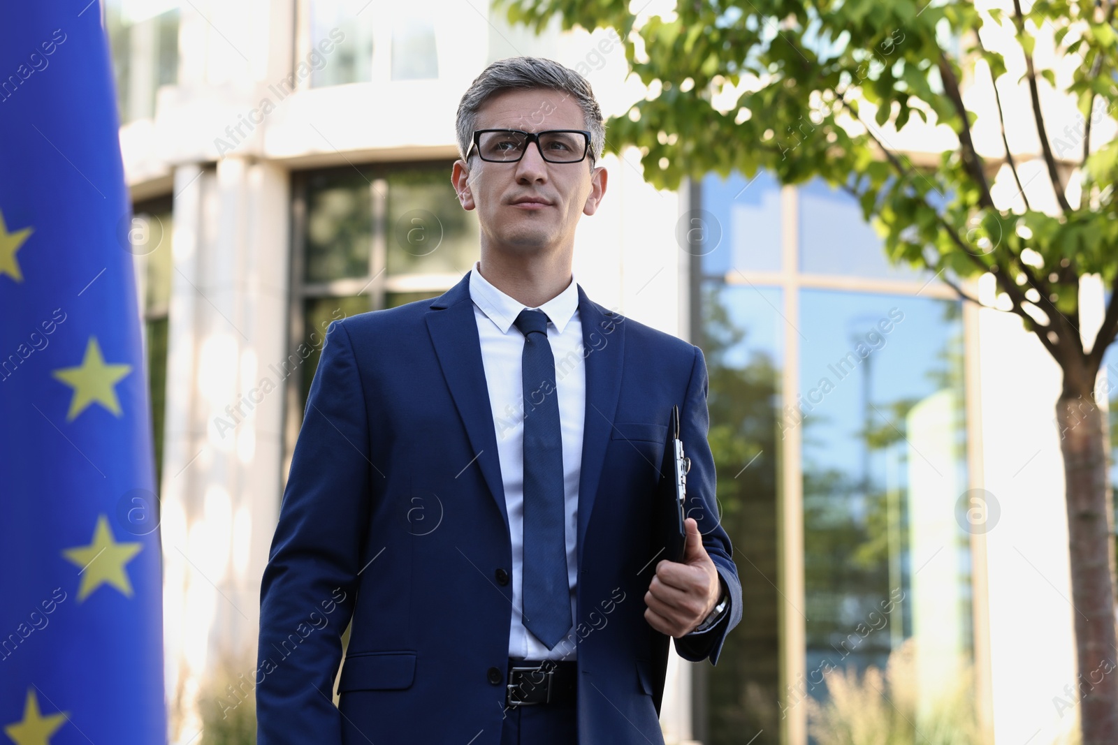 Photo of International relations. Diplomat with clipboard near flag of European Union outdoors