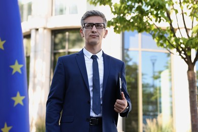 International relations. Diplomat with clipboard near flag of European Union outdoors