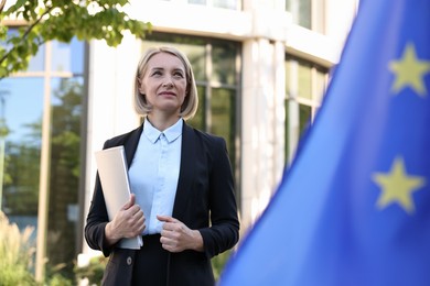 Photo of International relations. Diplomat with clipboard near flag of European Union outdoors