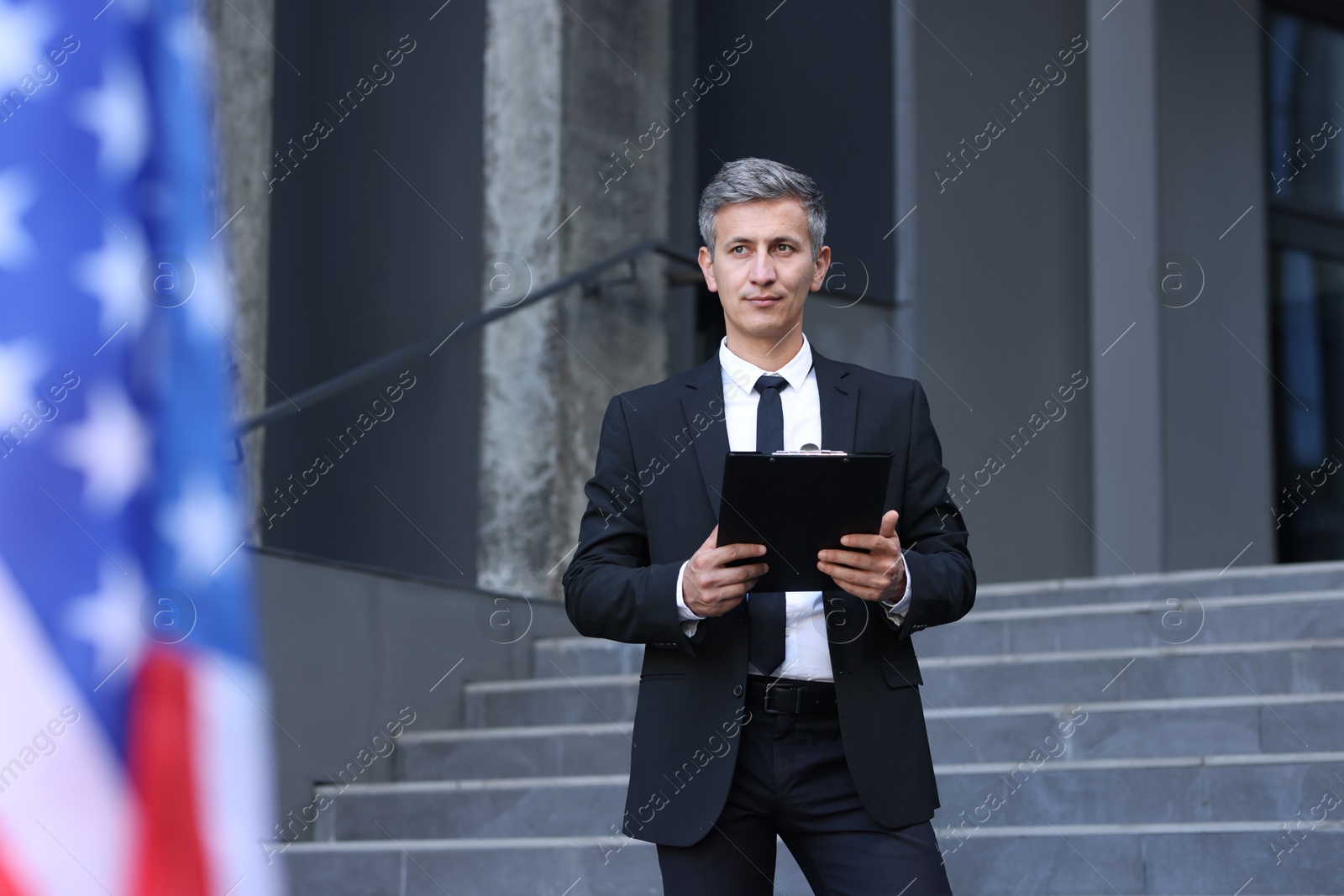 Photo of International relations. Diplomat with clipboard near flag of USA outdoors