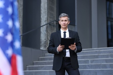 Photo of International relations. Diplomat with clipboard near flag of USA outdoors