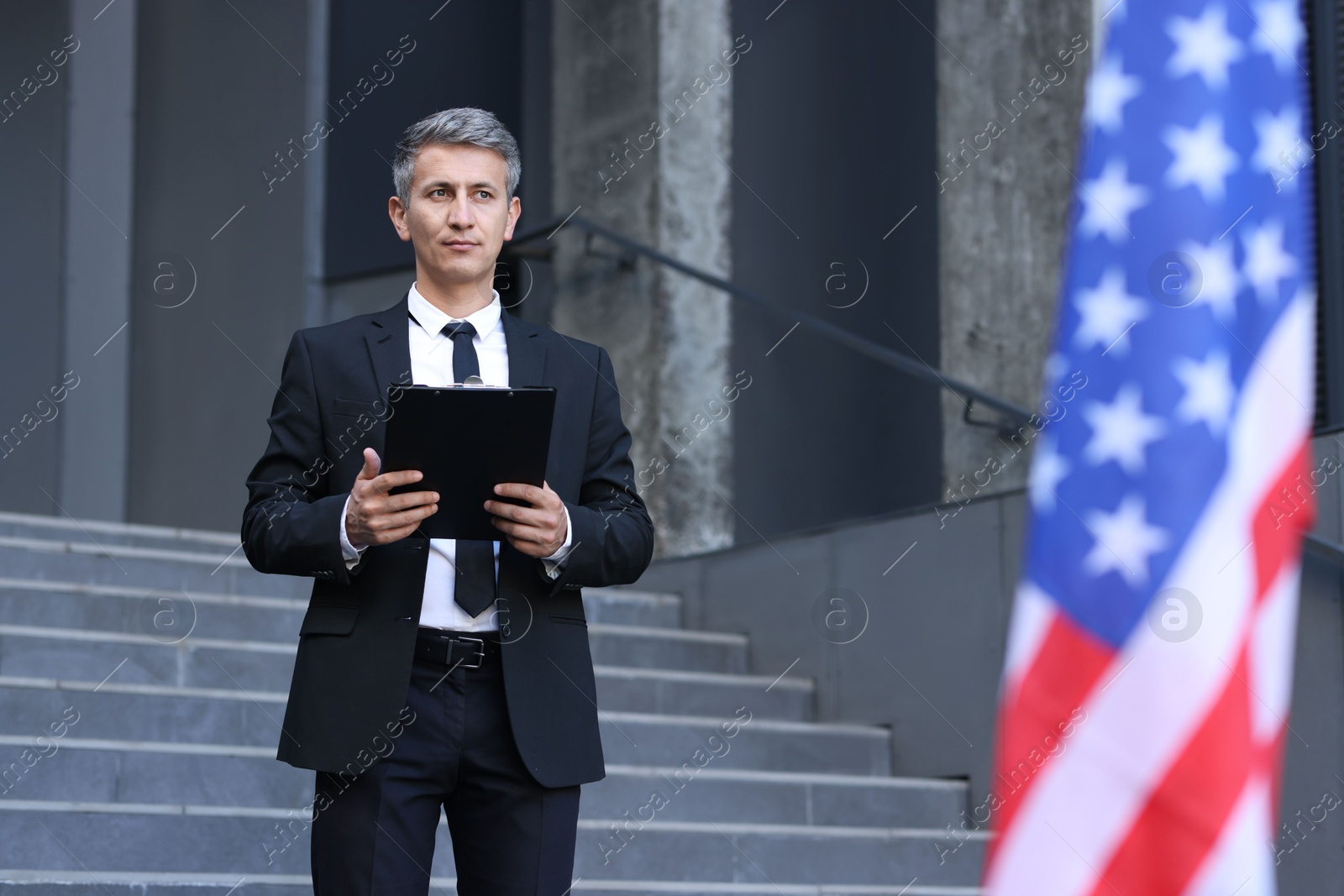 Photo of International relations. Diplomat with clipboard near flag of USA outdoors