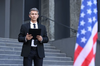 International relations. Diplomat with clipboard near flag of USA outdoors