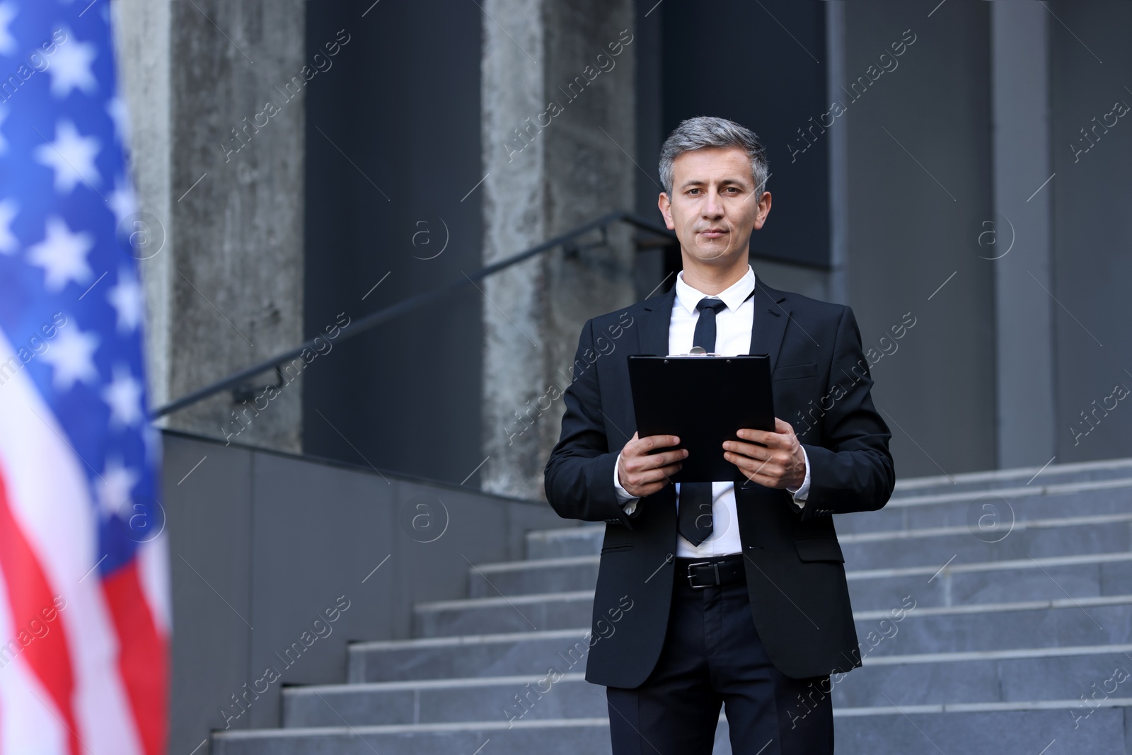 Photo of International relations. Diplomat with clipboard near flag of USA outdoors