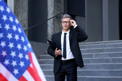 International relations. Diplomat with clipboard near flag of USA outdoors