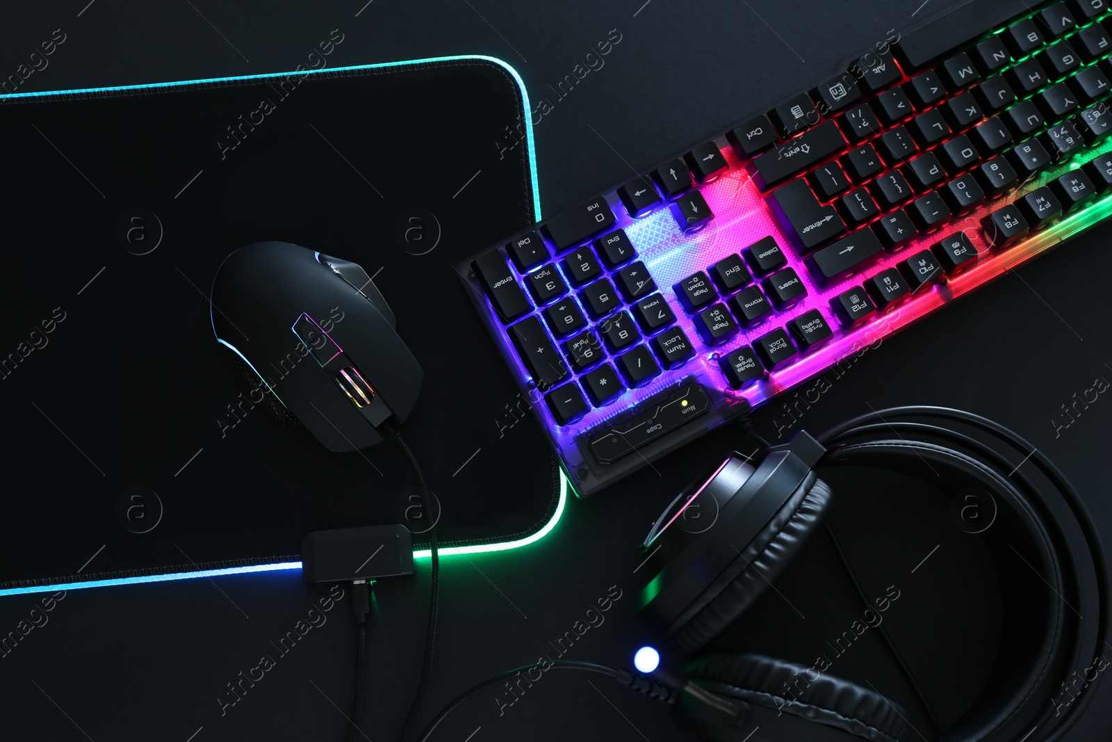 Photo of Computer mouse, RGB keyboard and headset on black background, flat lay