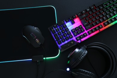 Photo of Computer mouse, RGB keyboard and headset on black background, flat lay