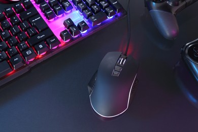 Photo of Computer mouse, RGB keyboard and game controllers in neon lights on dark background, above view