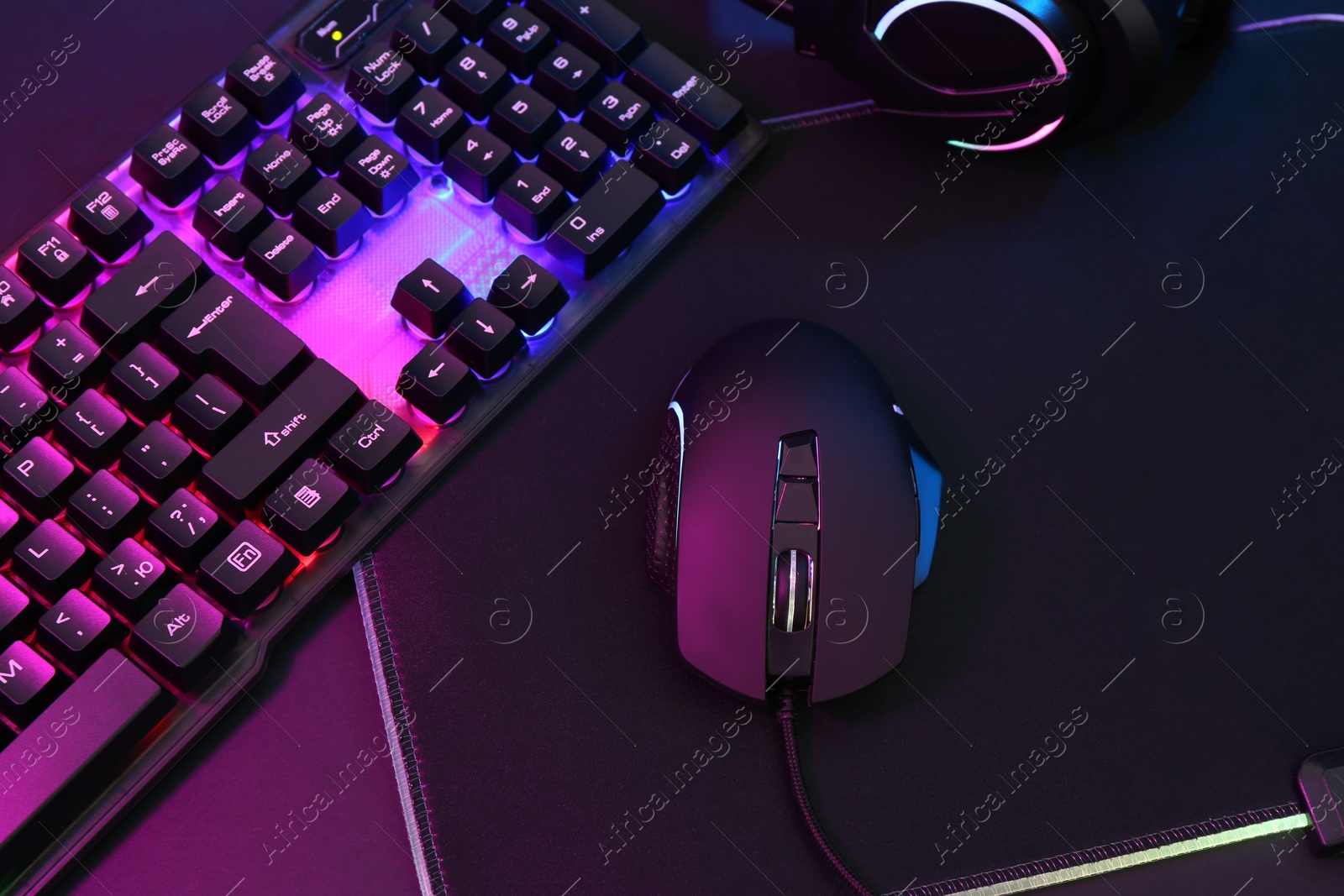 Photo of Computer mouse, headset and RGB keyboard in neon lights on dark background, above view