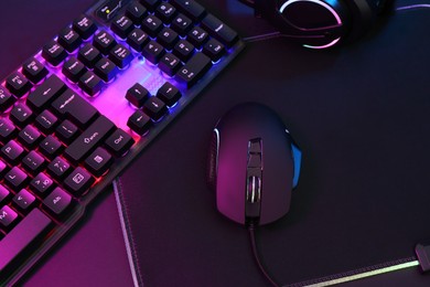 Photo of Computer mouse, headset and RGB keyboard in neon lights on dark background, above view