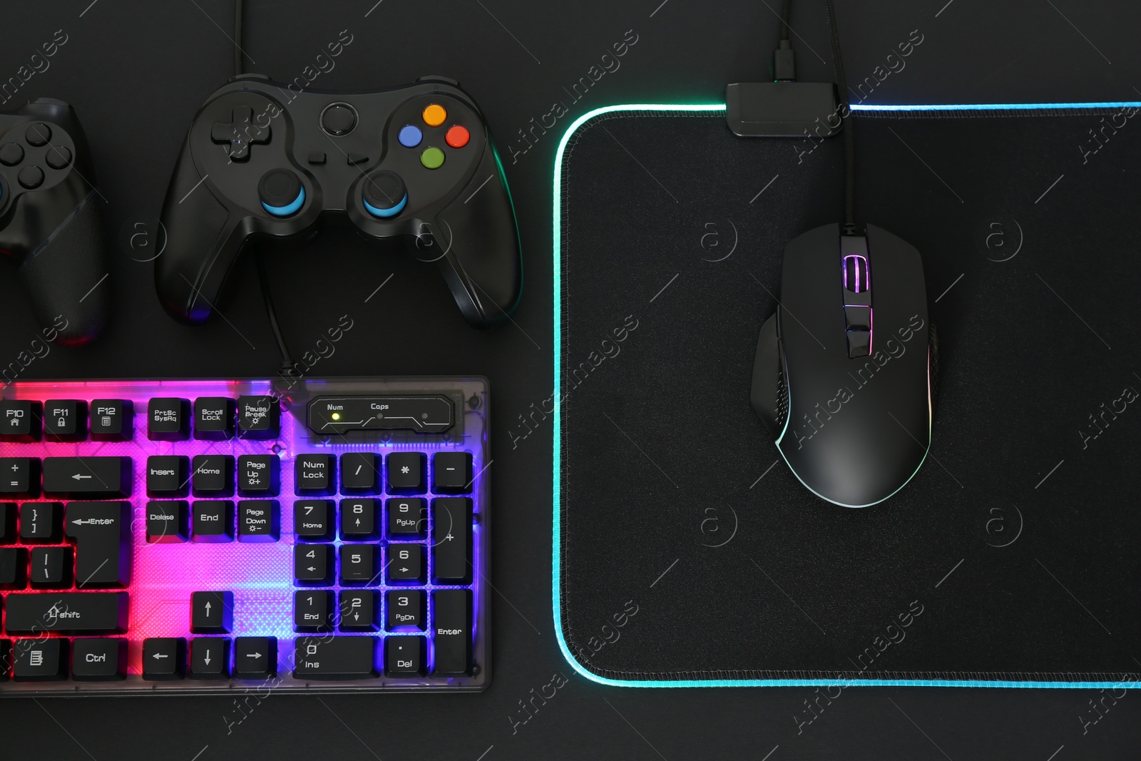 Photo of Computer mouse, RGB keyboard and game controllers on black background, flat lay