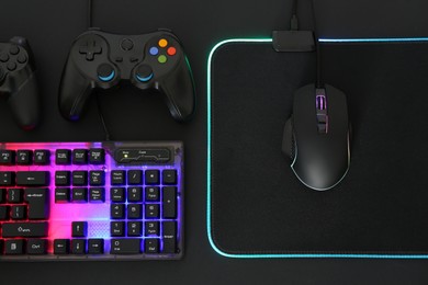 Computer mouse, RGB keyboard and game controllers on black background, flat lay