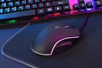 Photo of Computer mouse, mousepad and RGB keyboard on dark background, closeup