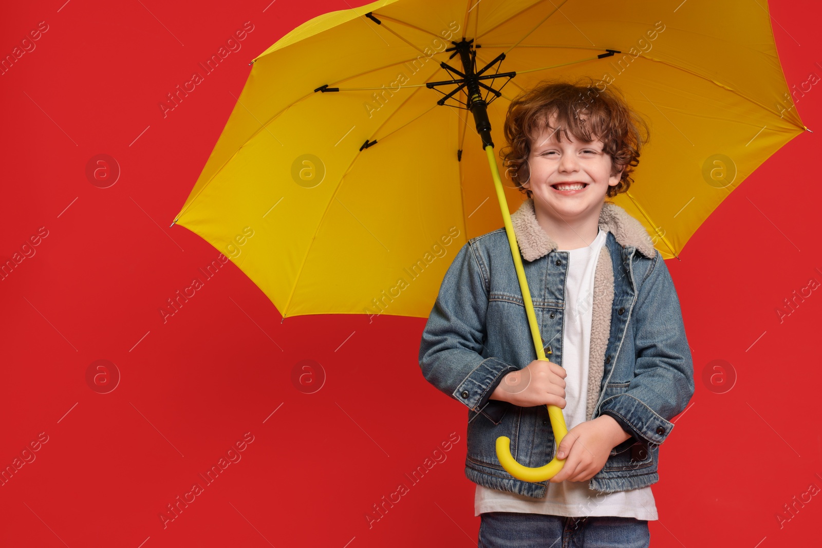 Photo of Little boy with yellow umbrella on red background