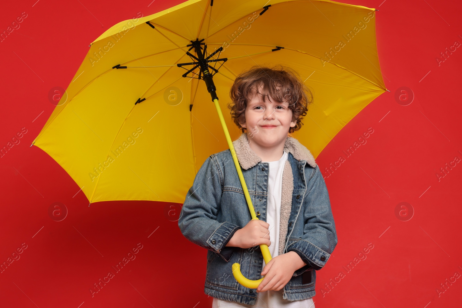 Photo of Little boy with yellow umbrella on red background