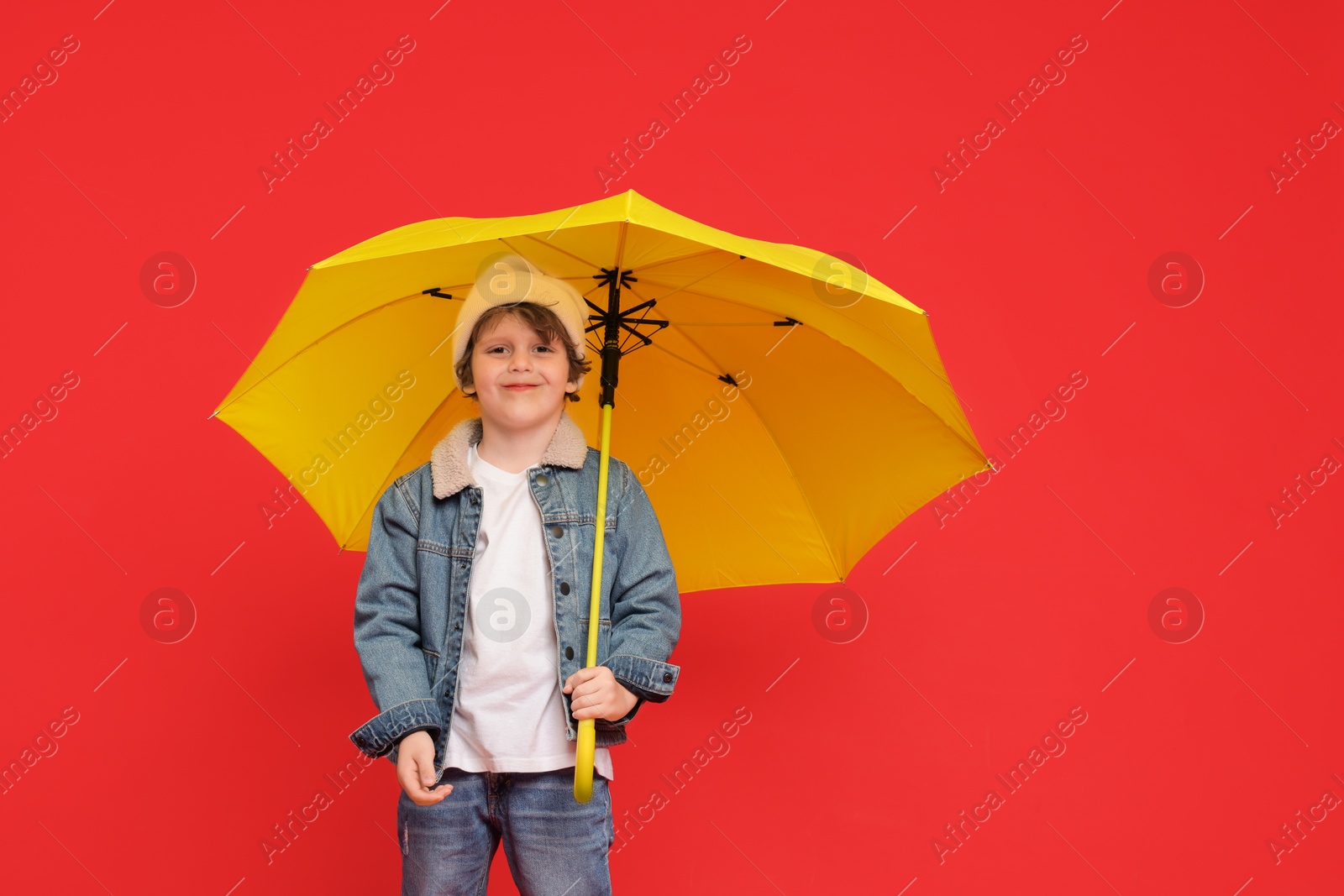 Photo of Little boy with yellow umbrella on red background, space for text