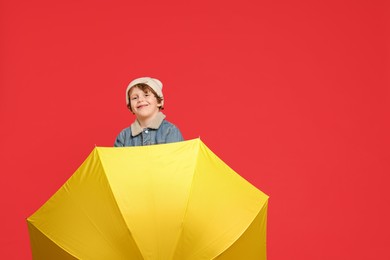 Little boy with yellow umbrella on red background, space for text