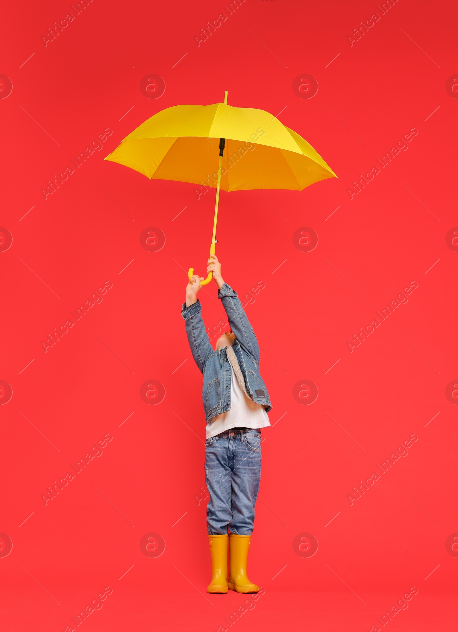 Photo of Little boy with yellow umbrella on red background, space for text