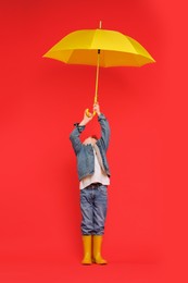 Little boy with yellow umbrella on red background, space for text