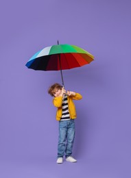 Little boy with rainbow umbrella on purple background