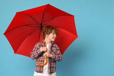 Little boy with red umbrella on light blue background, space for text