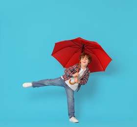 Photo of Little boy with red umbrella on light blue background