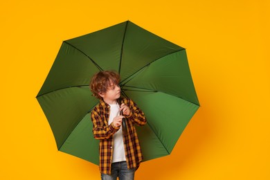 Little boy with green umbrella on orange background