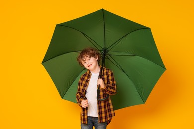 Photo of Little boy with green umbrella on orange background