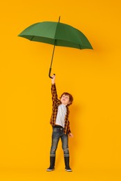 Little boy with green umbrella on orange background