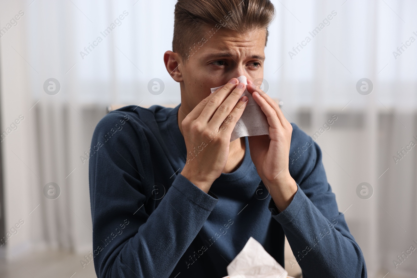 Photo of Young man with tissue suffering from sinusitis at wooden table indoors