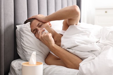 Young man with tissue suffering from sinusitis and lying in bed at home