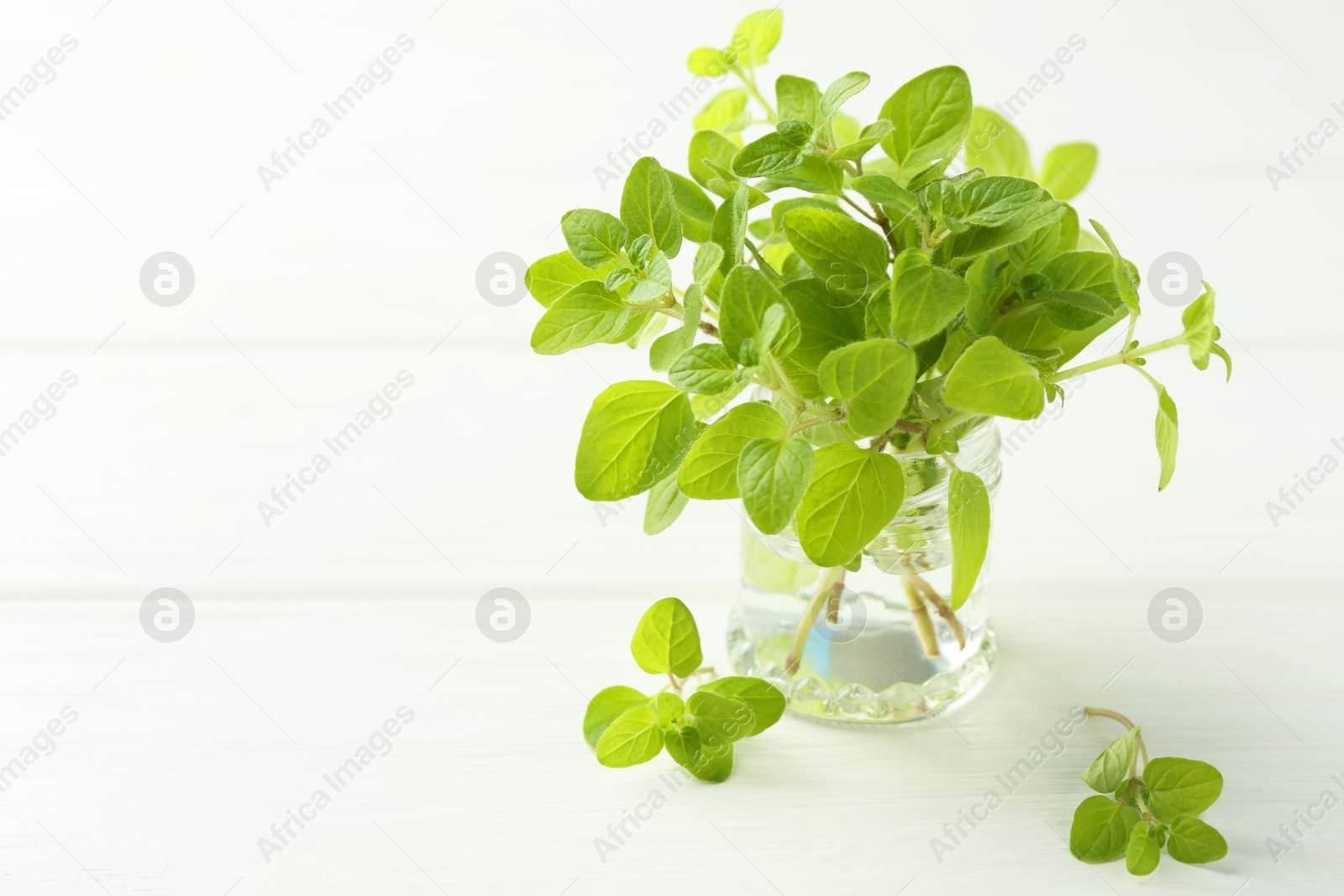 Photo of Sprigs of fresh green oregano in glass jar on white wooden table, space for text