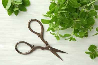 Photo of Sprigs of fresh green oregano and scissors on white wooden table, flat lay