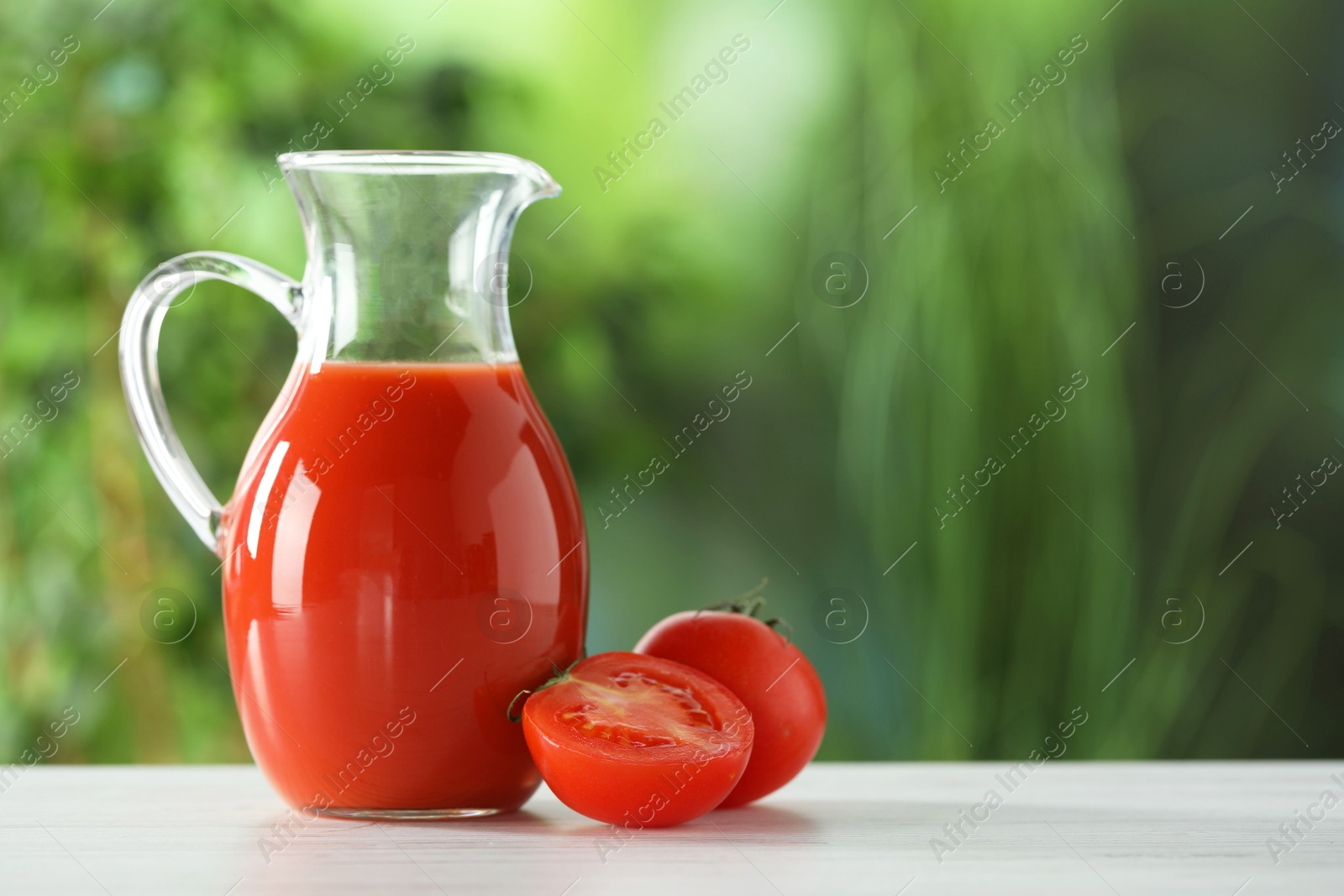 Photo of Tasty tomato juice in glass jug and fresh vegetables on white wooden table outdoors, space for text