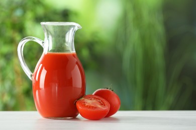 Photo of Tasty tomato juice in glass jug and fresh vegetables on white wooden table outdoors, space for text