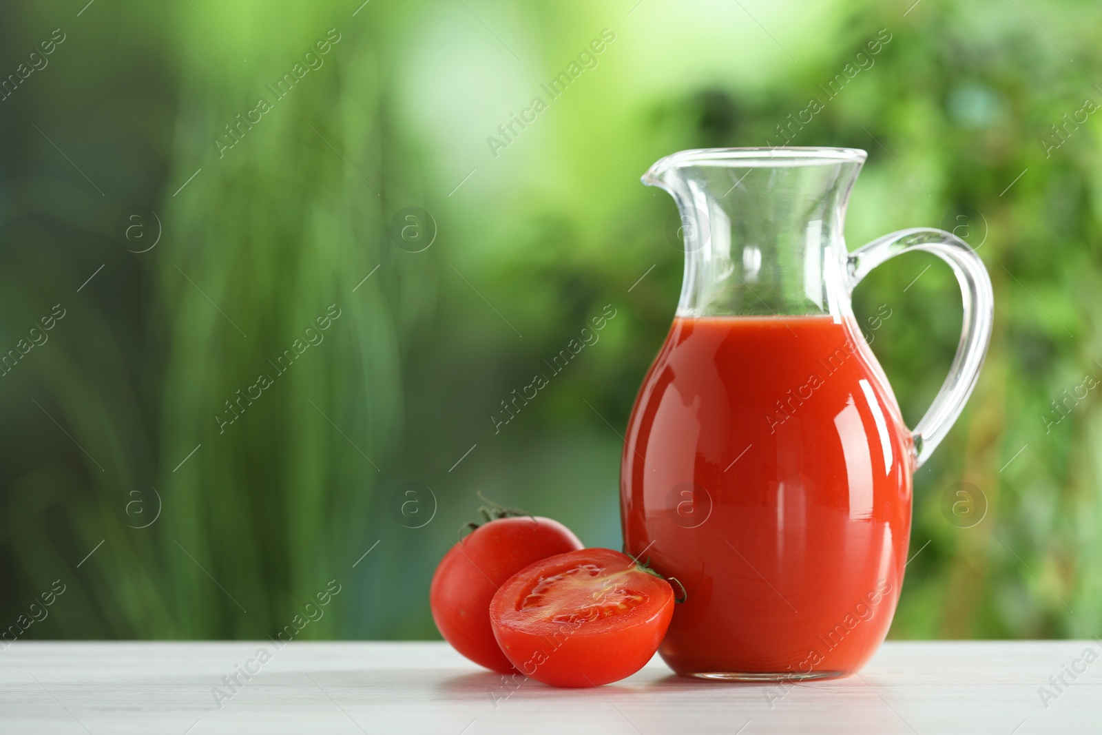 Photo of Tasty tomato juice in glass jug and fresh vegetables on white wooden table outdoors, space for text