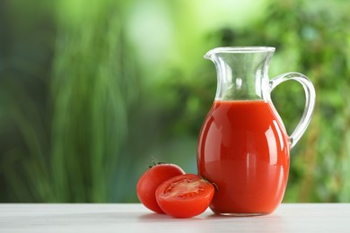 Photo of Tasty tomato juice in glass jug and fresh vegetables on white wooden table outdoors, space for text