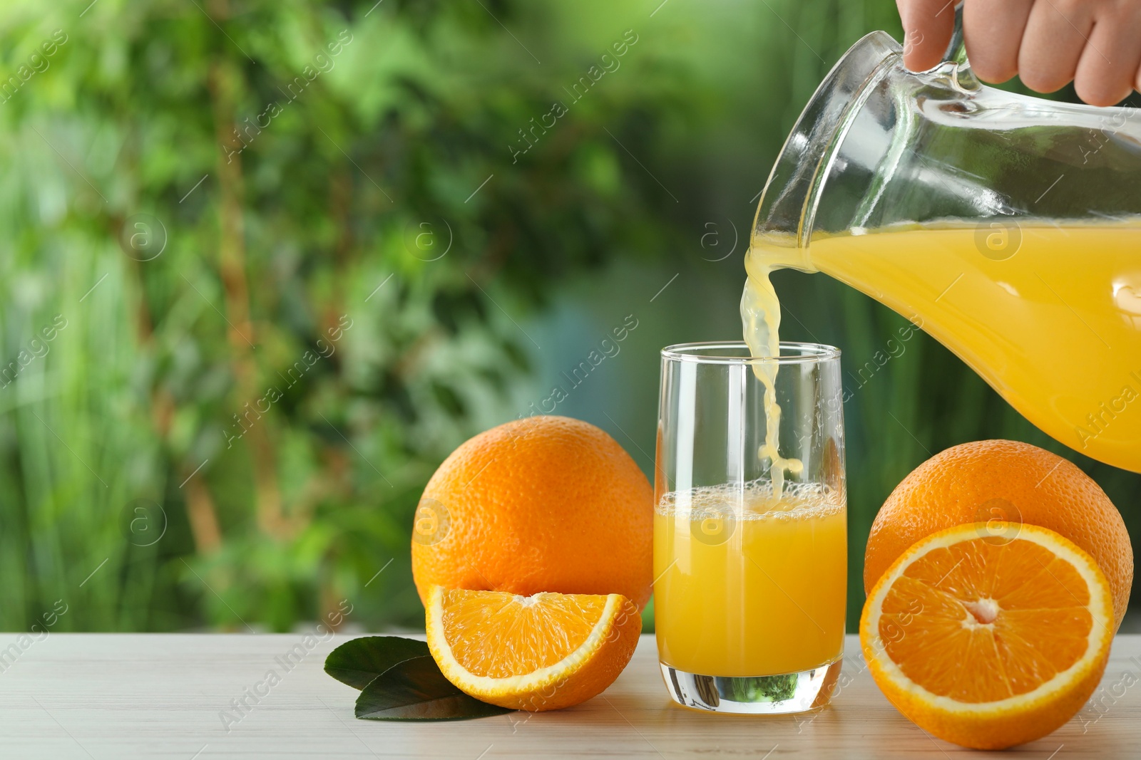 Photo of Woman pouring tasty orange juice into glass at white wooden table outdoors, closeup. Space for text