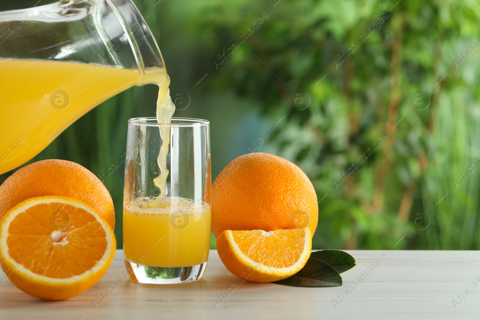 Photo of Woman pouring tasty orange juice into glass at white wooden table outdoors, closeup. Space for text