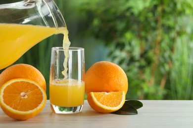 Photo of Woman pouring tasty orange juice into glass at white wooden table outdoors, closeup. Space for text