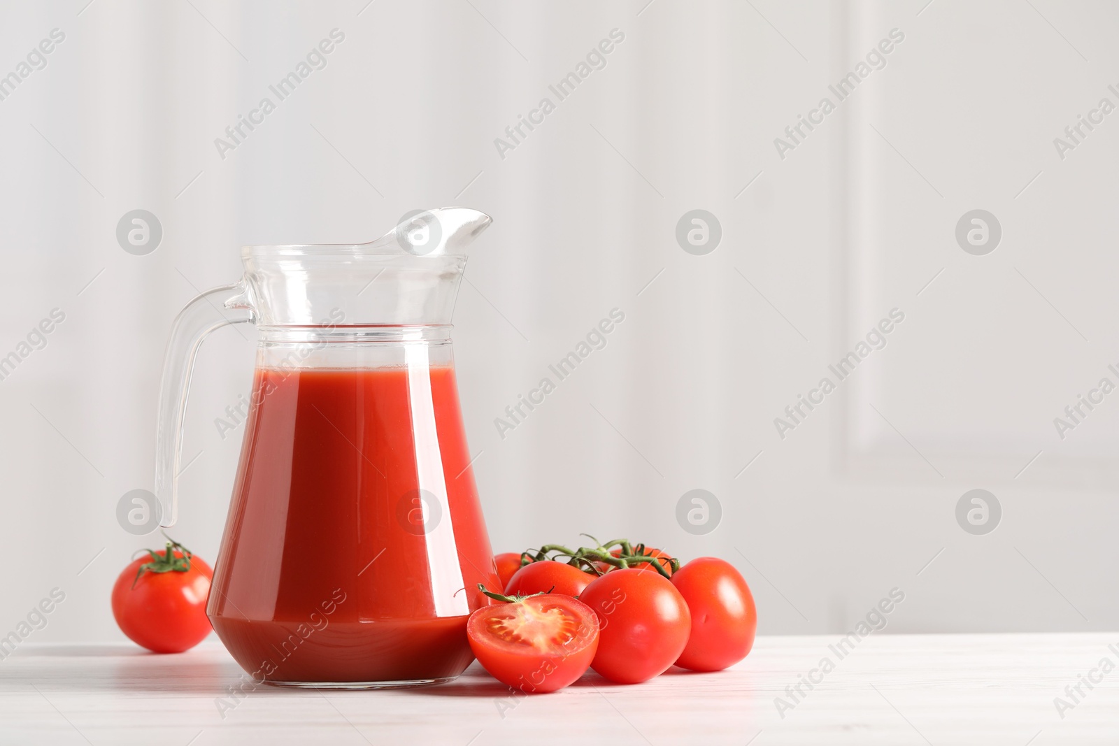 Photo of Tasty tomato juice in glass jug and fresh vegetables on white table. Space for text