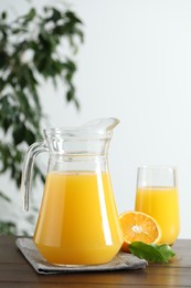 Tasty orange juice in jug, glass and citrus fruit on wooden table