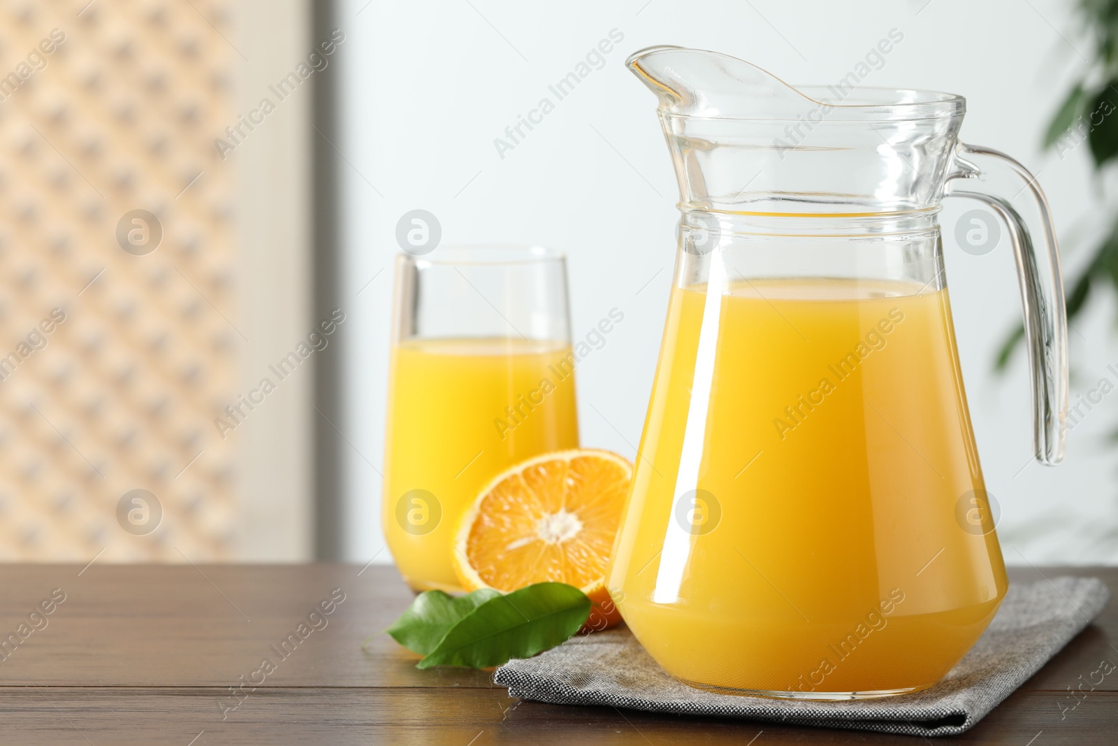 Photo of Tasty orange juice in jug, glass and citrus fruit on wooden table, closeup. Space for text