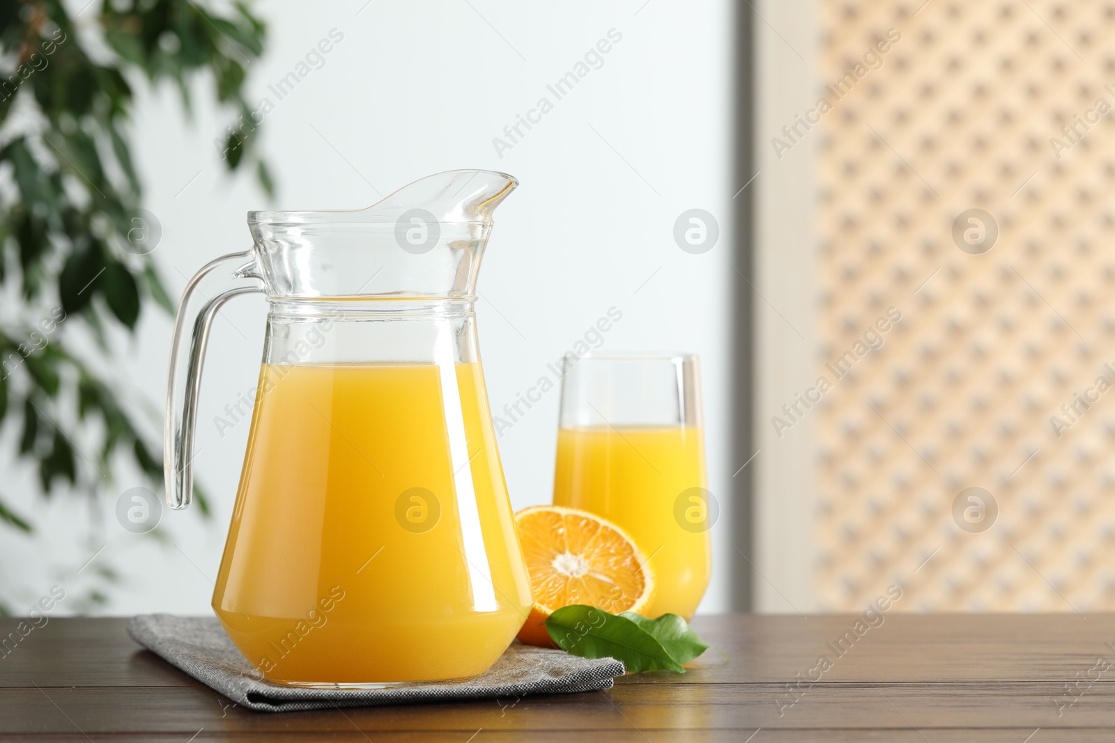 Photo of Tasty orange juice in jug, glass and citrus fruit on wooden table. Space for text