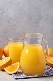 Tasty orange juice in jug, glass and citrus fruits on light table