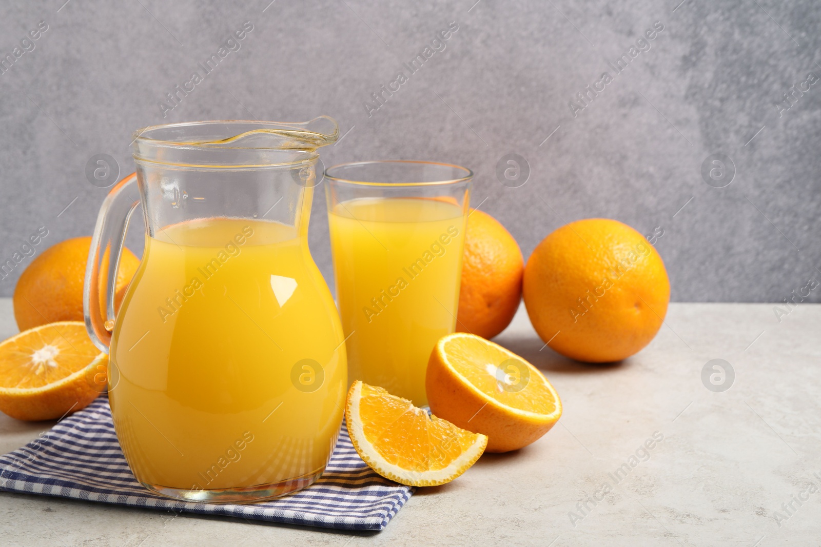 Photo of Tasty orange juice in jug, glass and citrus fruits on light table. Space for text