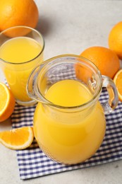 Photo of Tasty orange juice in jug, glass and citrus fruits on light table