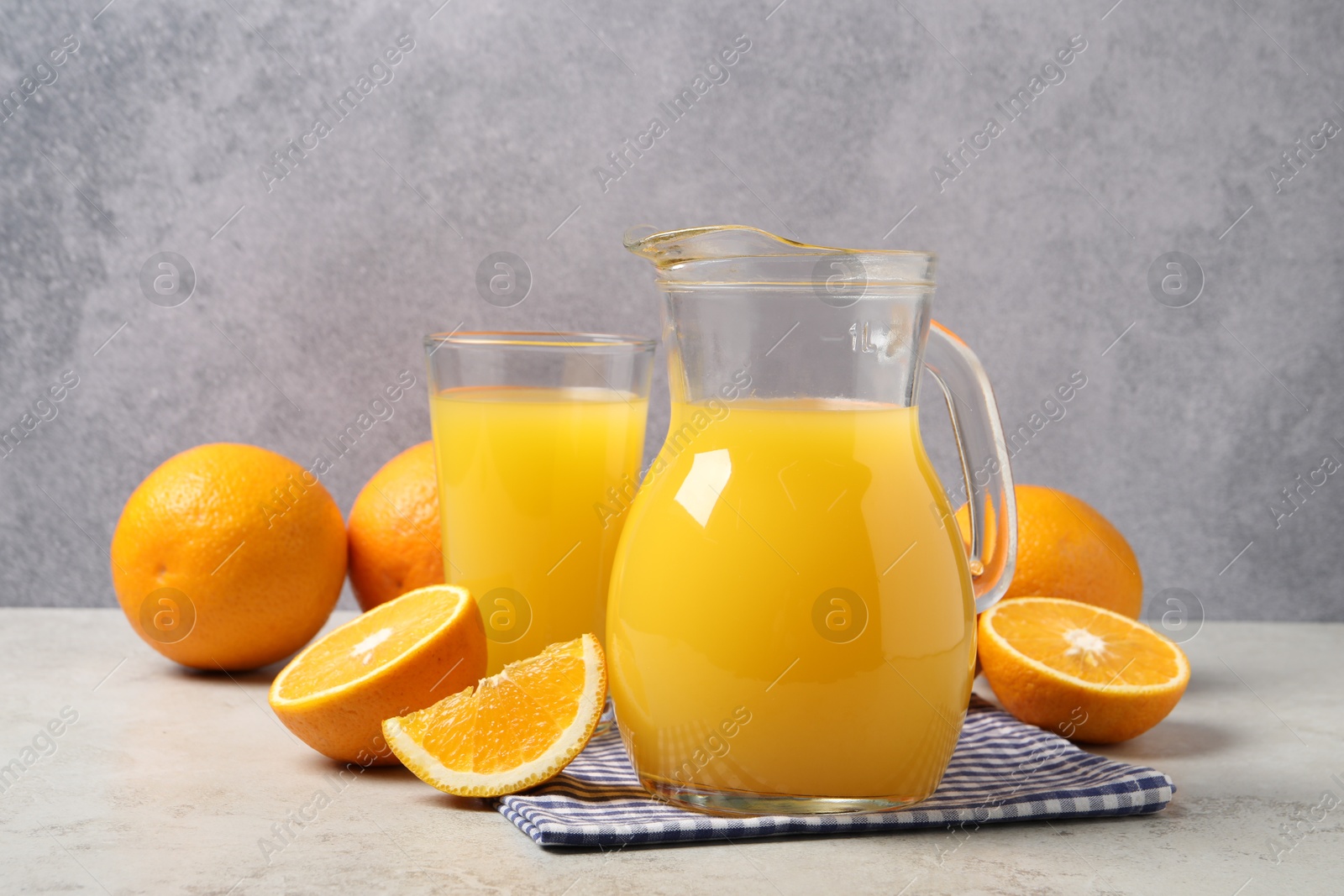 Photo of Tasty orange juice in jug, glass and citrus fruits on light table