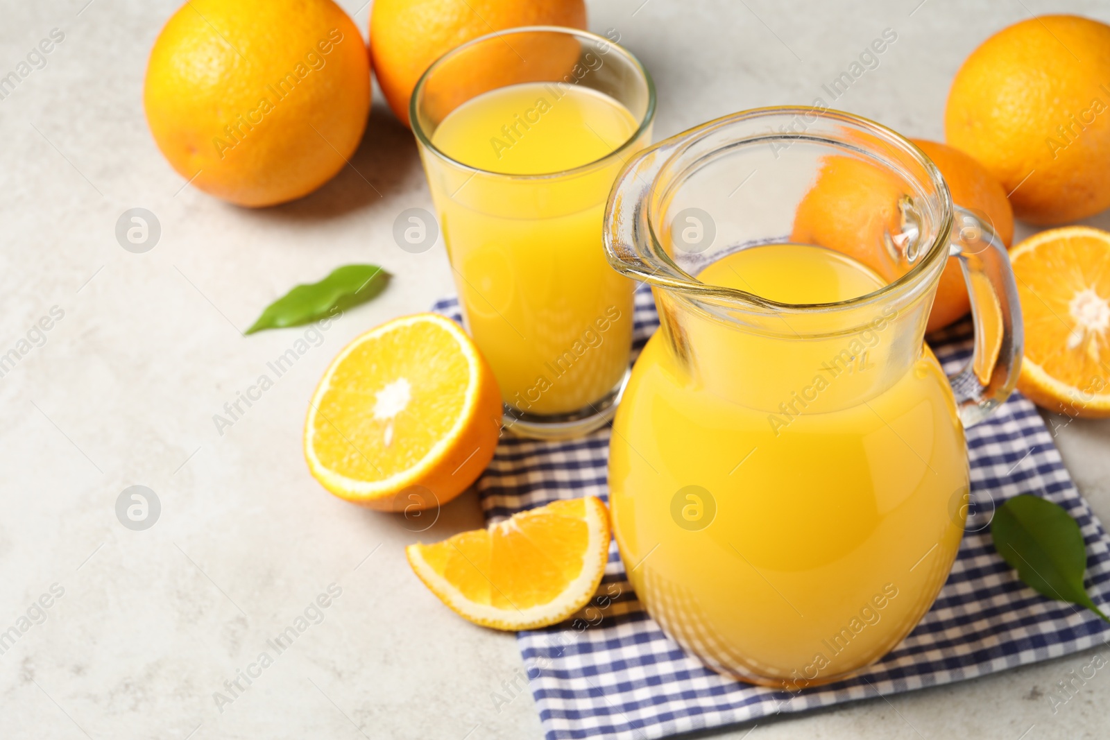 Photo of Tasty orange juice in jug, glass and citrus fruits on light textured table. Space for text